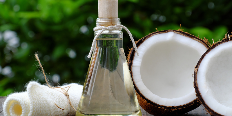 Frasco de óleo de coco natural e coco fresco, ingredientes utilizados no shampoo caseiro para fortalecer os fios, promovendo hidratação e nutrição profunda.