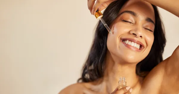 Mulher sorridente aplicando serum de rosa mosqueta no rosto, destacando os benefícios de hidratação e rejuvenescimento para uma pele saudável.