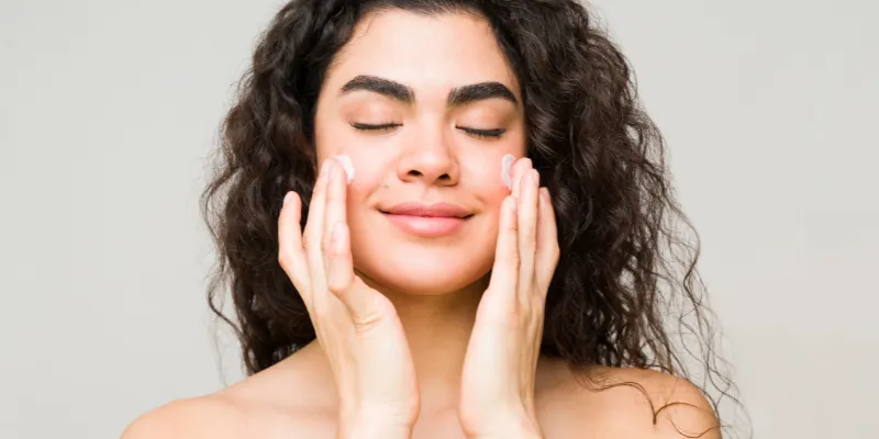 Mulher aplicando hidratante facial, destacando a sensação de pele saudável e revitalizada após a aplicação de produtos anti-idade com ácido hialurônico.