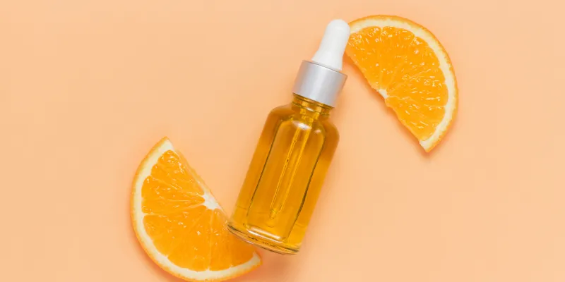 Frasco de sérum facial de vitamina C ao lado de fatias de laranja, representando os benefícios antioxidantes e revitalizantes da vitamina C no cuidado com a pele sensível.