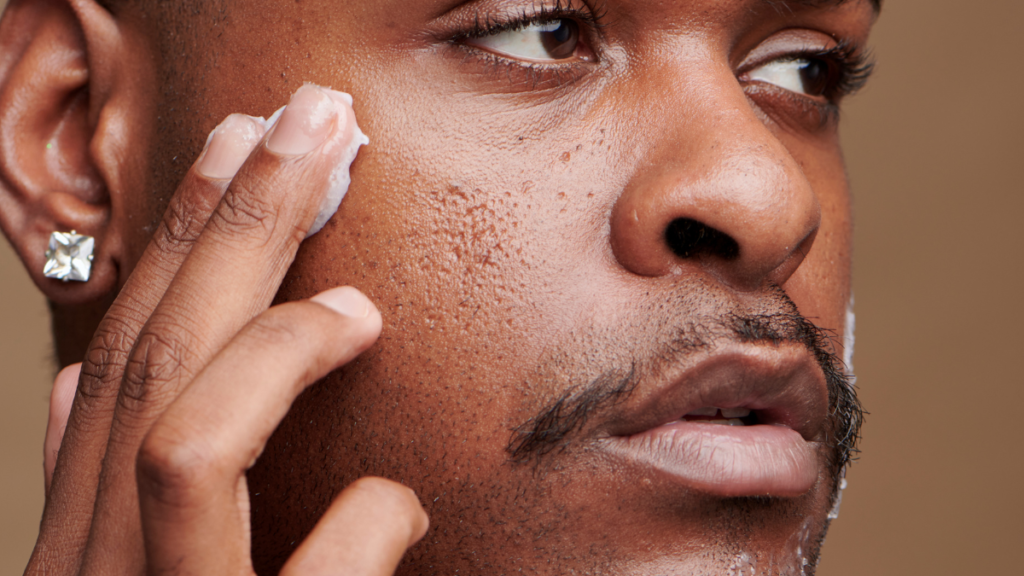 Homem aplicando creme facial, demonstrando cuidado com a pele masculina para reduzir linhas de expressão e melhorar a hidratação.