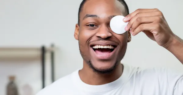 Homem sorrindo enquanto aplica produtos de skincare masculino para cuidados faciais