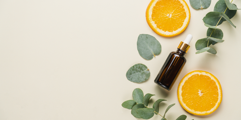 Frasco de sérum de vitamina C ao lado de rodelas de laranja e folhas de eucalipto, representando os benefícios naturais da vitamina C para a pele sensível no skincare.